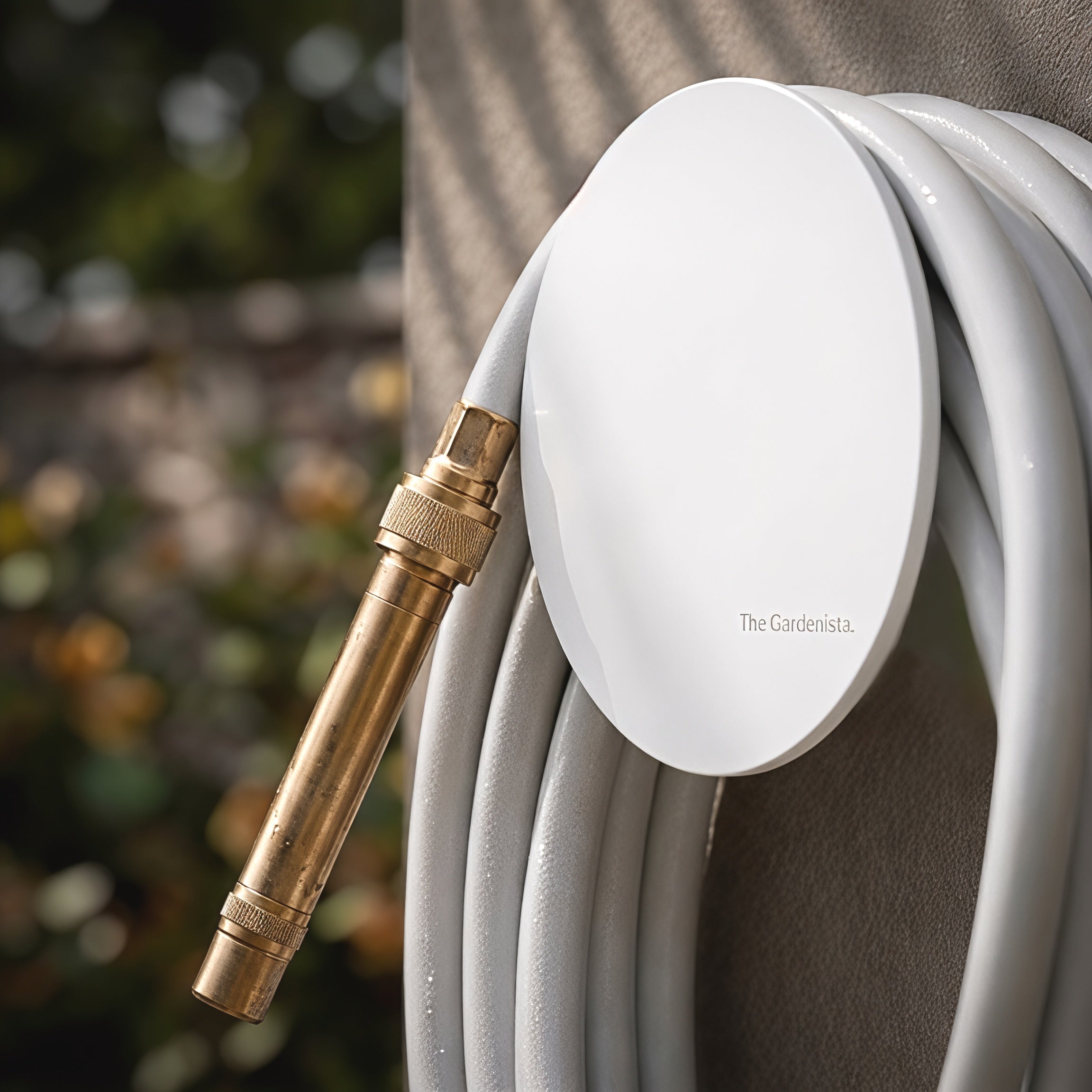 Close-up of soft grey hybrid garden hose on a white hose holder, showing solid brass fittings and engraved The Gardenista logo.