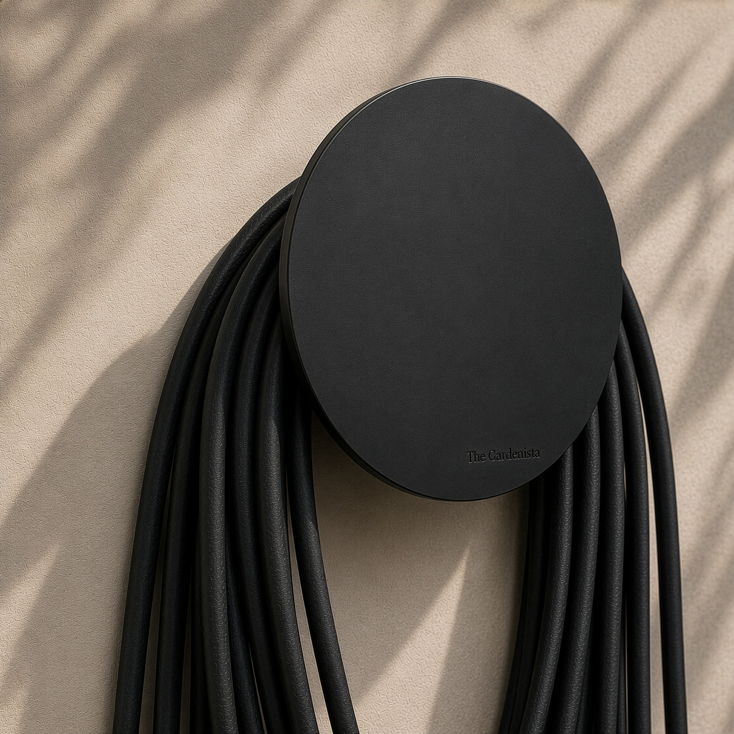 Large black wall-mounted hose holder with coiled black garden hose on a warm rendered wall.