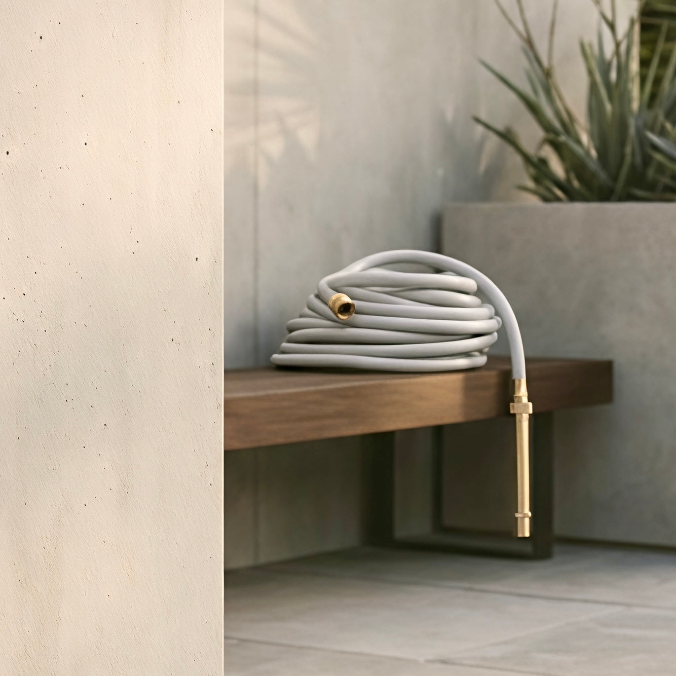 Soft grey hybrid garden hose casually coiled on a timber garden bench with brass nozzle hanging over the edge.
