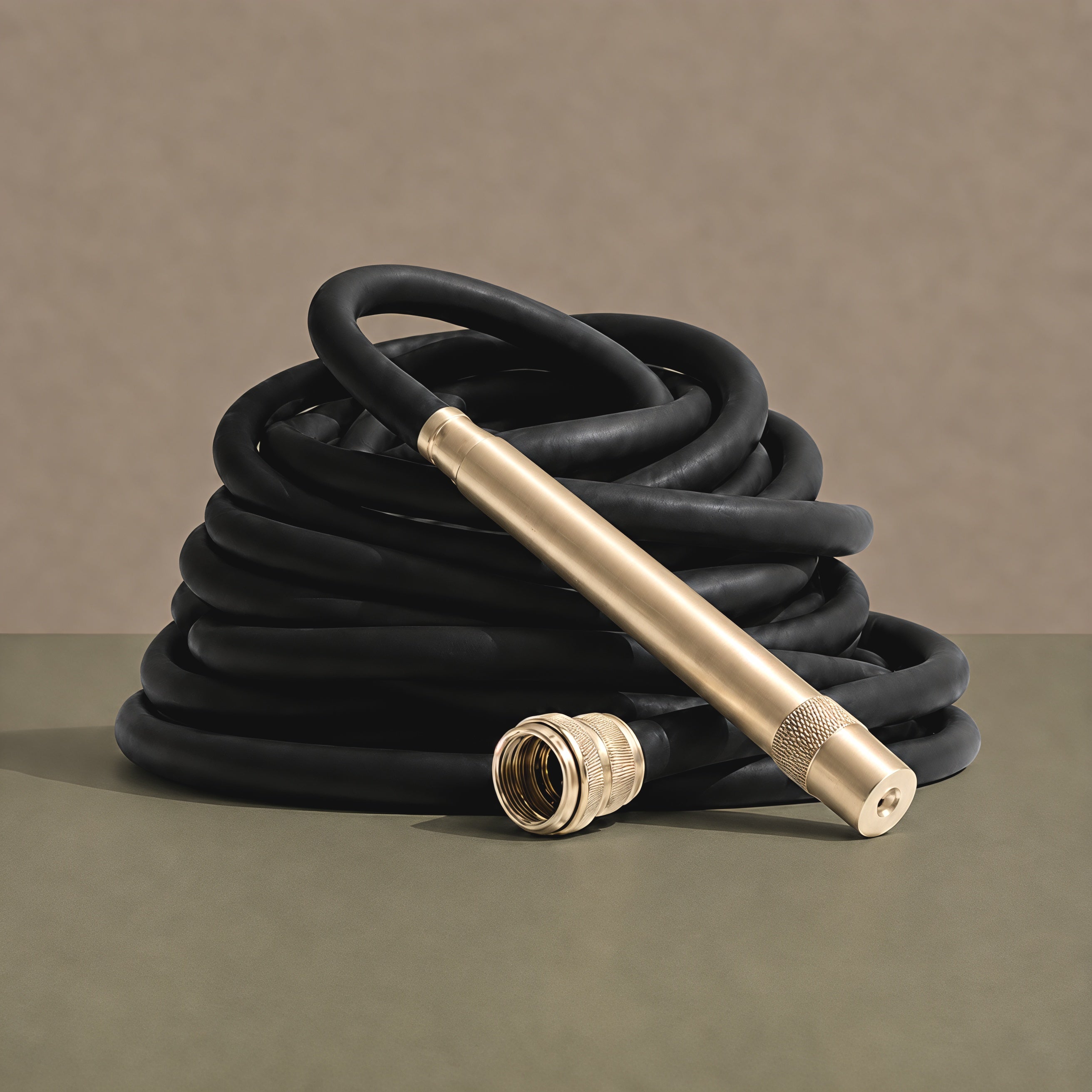 Matte black hybrid garden hose coiled with solid brass fittings and brass torch nozzle against a warm neutral background.