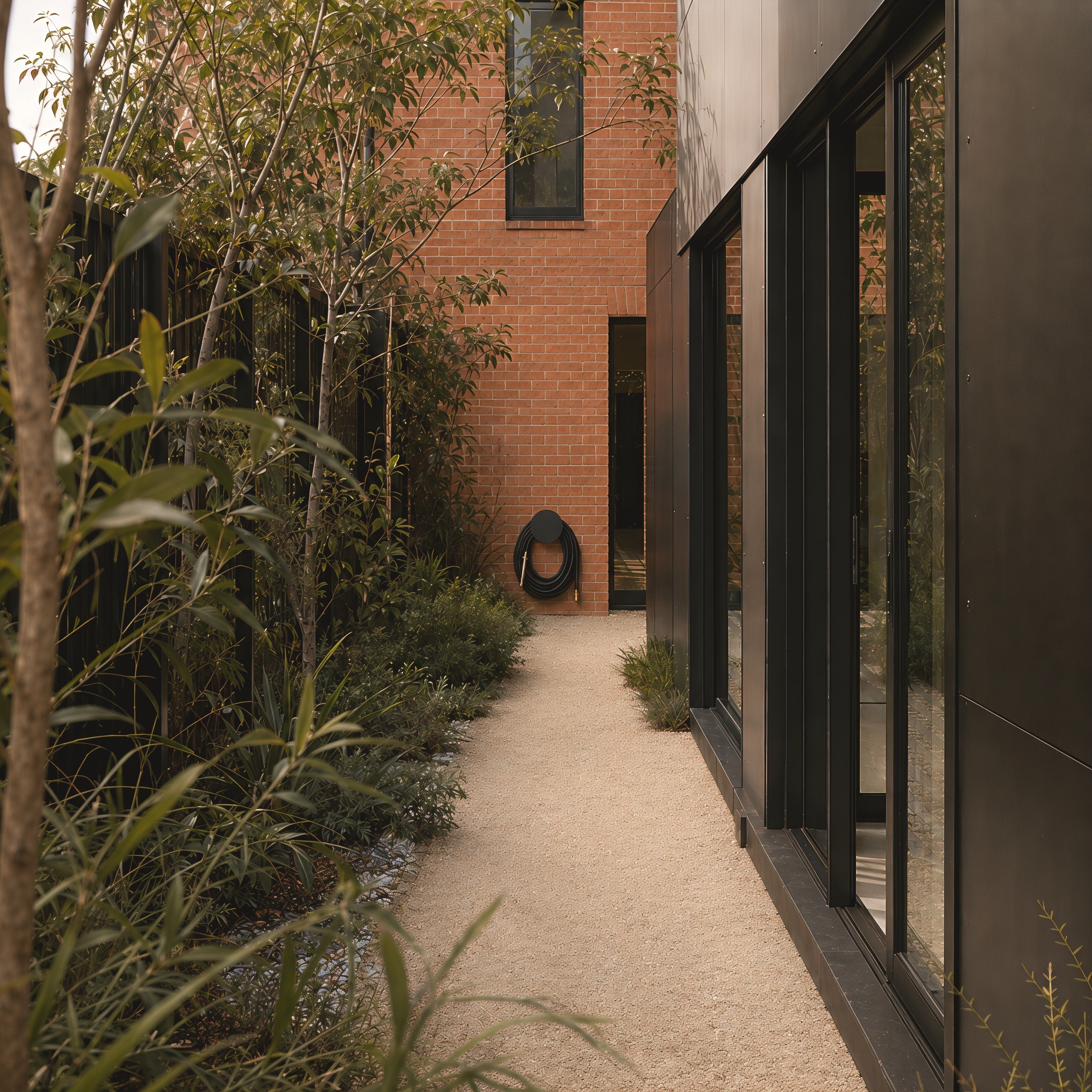 Matte black hybrid garden hose and black hose holder in a contemporary architectural garden setting.