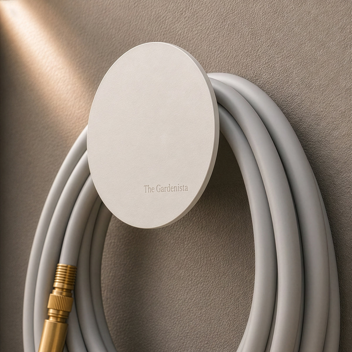 Small white wall-mounted hose holder with pale grey garden hose and brass fittings.